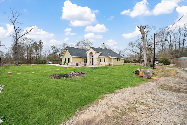 back of house with stone siding, a lawn, a chimney, and fence