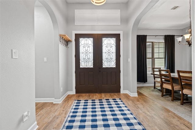 foyer with arched walkways, baseboards, visible vents, and light wood-style floors