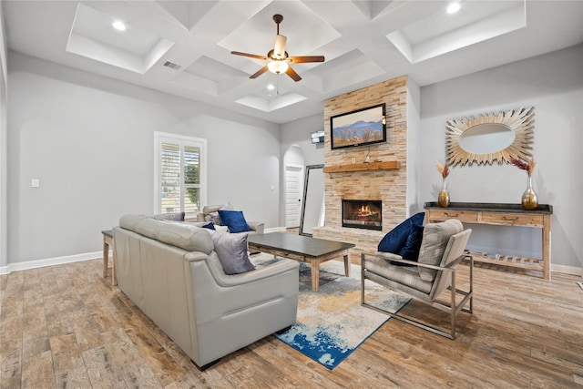 living room featuring arched walkways, a fireplace, visible vents, light wood-style flooring, and baseboards