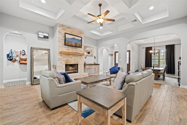 living area with light wood finished floors, baseboards, visible vents, arched walkways, and a stone fireplace