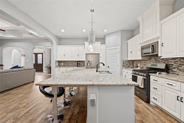 kitchen with hanging light fixtures, appliances with stainless steel finishes, open floor plan, a kitchen island with sink, and a sink