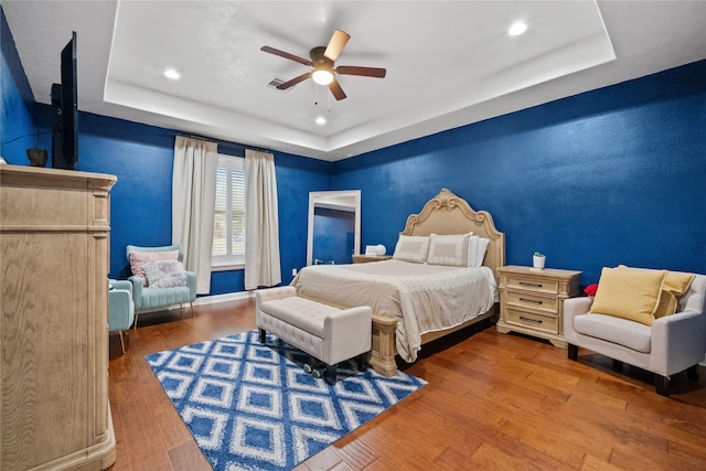 bedroom featuring a raised ceiling, ceiling fan, and wood finished floors