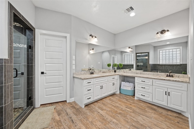 full bath with double vanity, a sink, visible vents, and wood finished floors