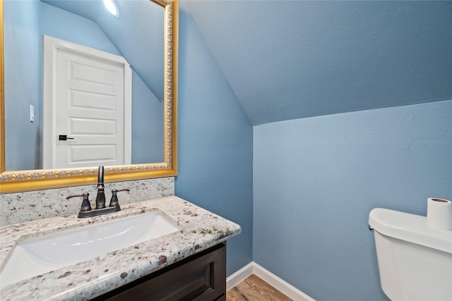 bathroom featuring lofted ceiling, toilet, vanity, wood finished floors, and baseboards