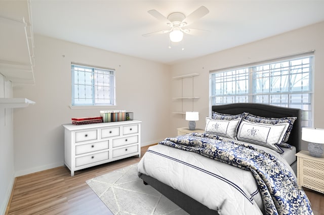 bedroom featuring a ceiling fan, multiple windows, baseboards, and wood finished floors