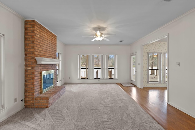 unfurnished living room with crown molding, a brick fireplace, ceiling fan, wood finished floors, and baseboards