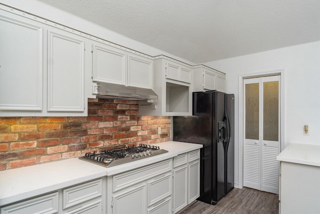 kitchen with light countertops, black fridge with ice dispenser, stainless steel gas stovetop, white cabinetry, and under cabinet range hood