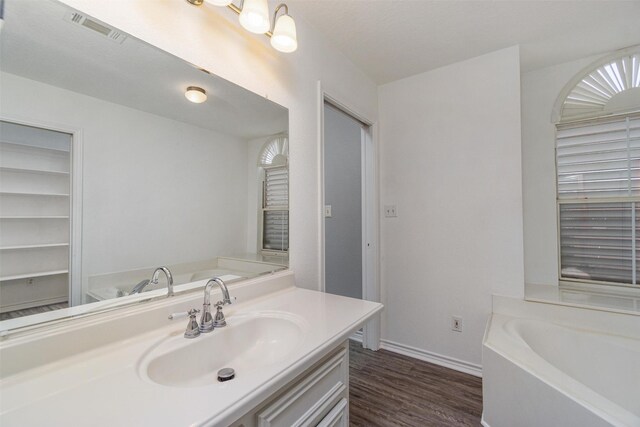 bathroom featuring a garden tub, wood finished floors, vanity, visible vents, and baseboards