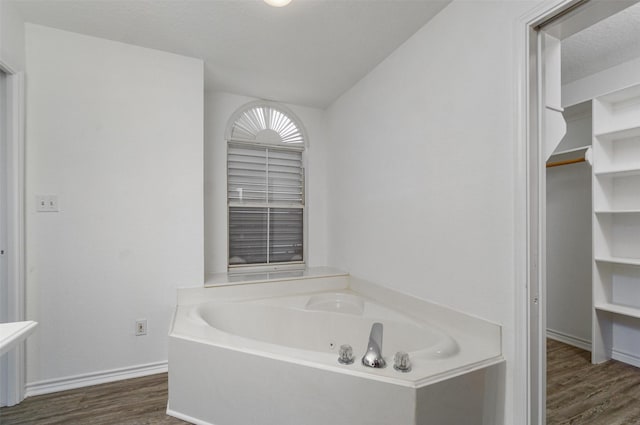 bathroom featuring a garden tub, a textured ceiling, baseboards, and wood finished floors