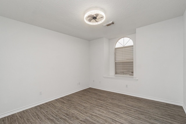 empty room featuring dark wood-style floors, a textured ceiling, visible vents, and baseboards
