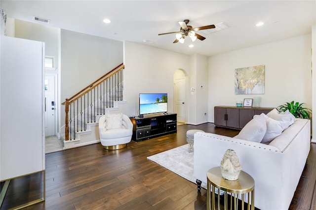 living room featuring arched walkways, dark wood-style flooring, recessed lighting, visible vents, and stairway