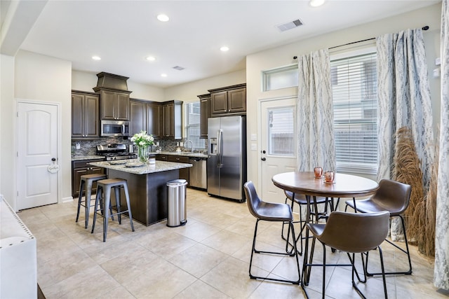 kitchen with dark brown cabinetry, stainless steel appliances, a center island, visible vents, and decorative backsplash