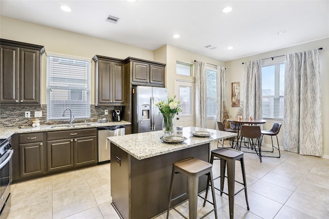 kitchen with stainless steel appliances, dark brown cabinetry, a kitchen island, and a sink