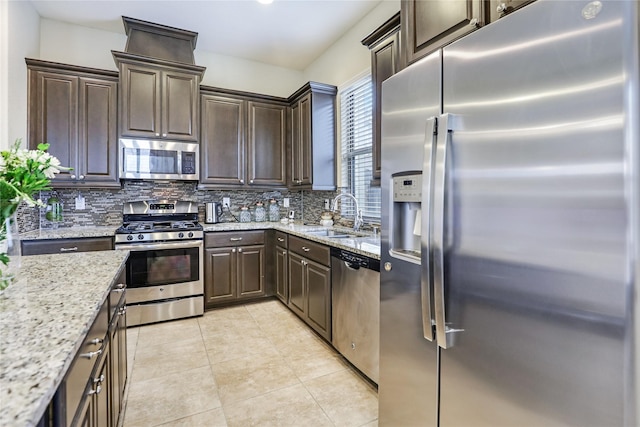 kitchen with stainless steel appliances, a sink, decorative backsplash, and light stone countertops