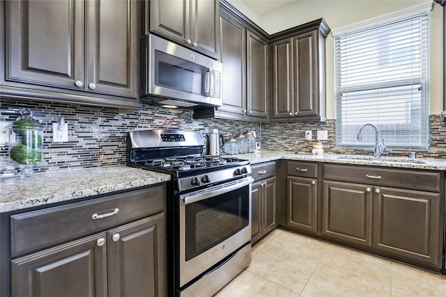 kitchen with light tile patterned floors, stainless steel appliances, backsplash, a sink, and dark brown cabinets