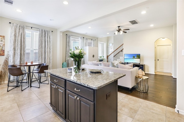 kitchen with a center island, arched walkways, light tile patterned floors, visible vents, and open floor plan