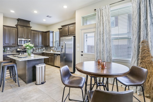 kitchen featuring dark brown cabinetry, a kitchen island, visible vents, appliances with stainless steel finishes, and tasteful backsplash