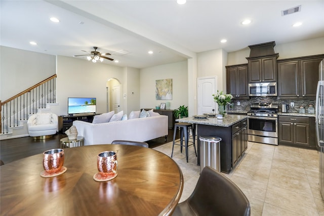 dining area featuring arched walkways, recessed lighting, visible vents, a ceiling fan, and stairs