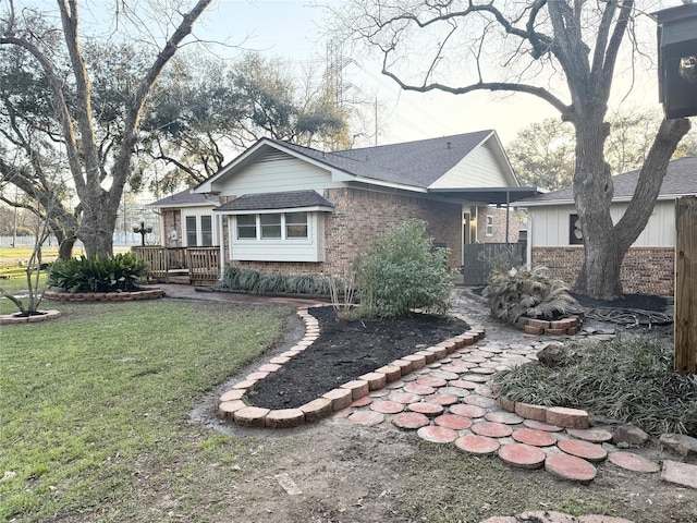 ranch-style house with brick siding, roof with shingles, a front yard, and a wooden deck