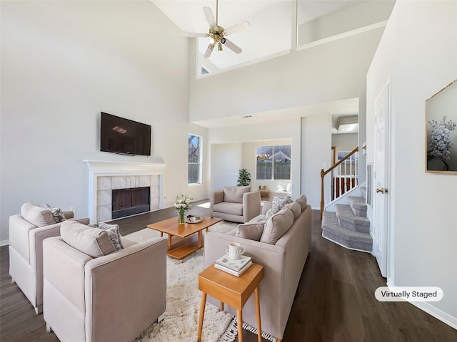 living room with baseboards, a ceiling fan, a tiled fireplace, dark wood-type flooring, and stairs