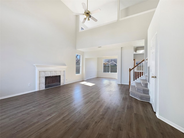 unfurnished living room with dark wood-style floors, stairway, a ceiling fan, and a tile fireplace