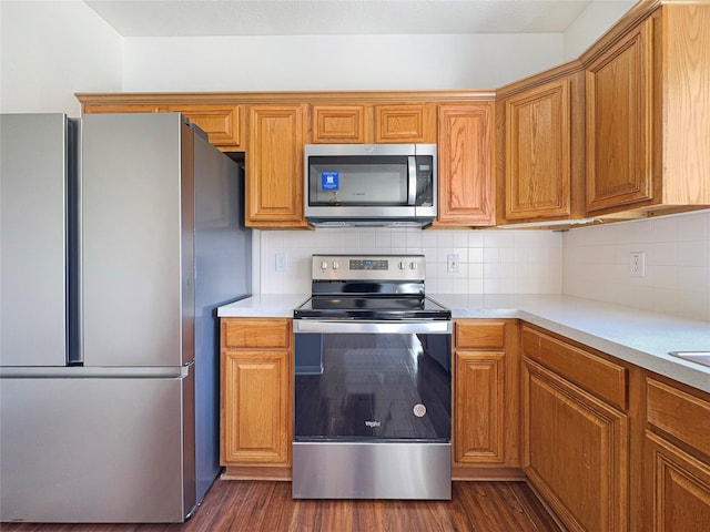 kitchen featuring stainless steel appliances, brown cabinetry, light countertops, and dark wood-type flooring