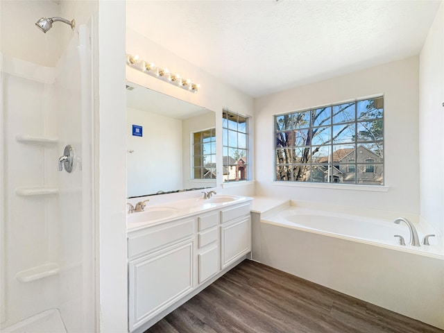 full bath with a garden tub, a textured ceiling, a sink, and wood finished floors