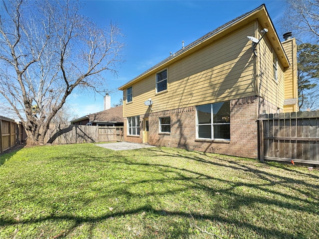 rear view of property featuring a patio, a fenced backyard, a chimney, a yard, and brick siding