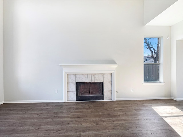 unfurnished living room with baseboards, dark wood-style flooring, and a tile fireplace