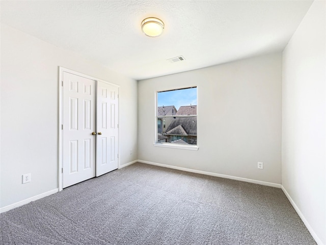 empty room with a textured ceiling, carpet, visible vents, and baseboards