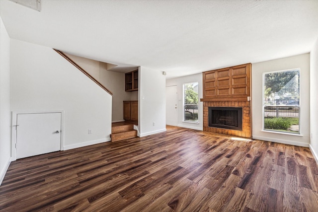 unfurnished living room featuring dark wood-style flooring, a brick fireplace, and a healthy amount of sunlight