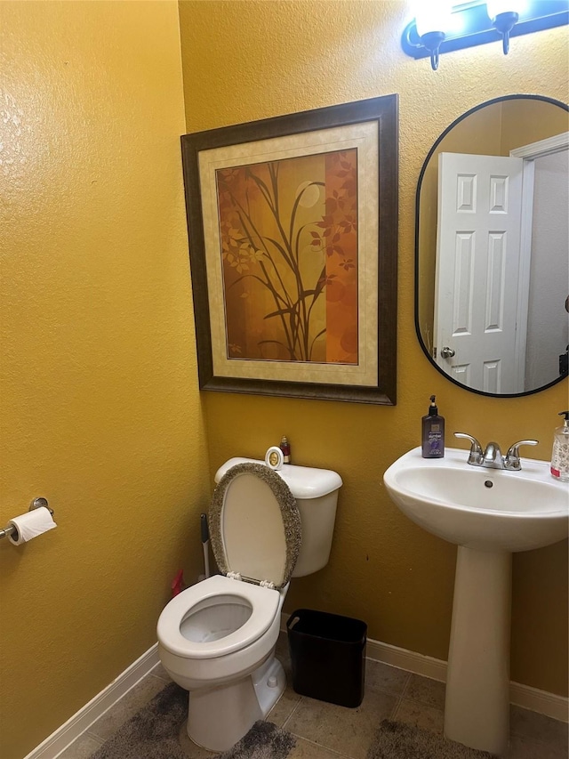 bathroom featuring toilet, baseboards, a sink, and tile patterned floors