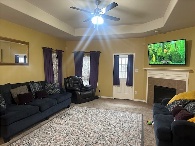 living room with light carpet, a ceiling fan, baseboards, a tray ceiling, and a tiled fireplace