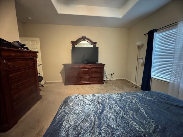 bedroom featuring light carpet, a raised ceiling, and baseboards