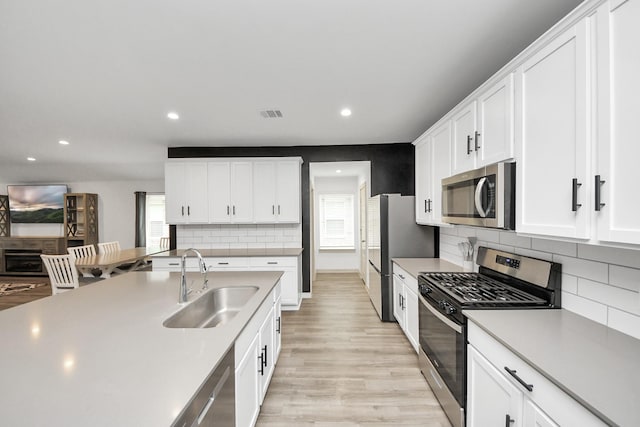 kitchen featuring appliances with stainless steel finishes, light countertops, light wood-type flooring, white cabinetry, and a sink