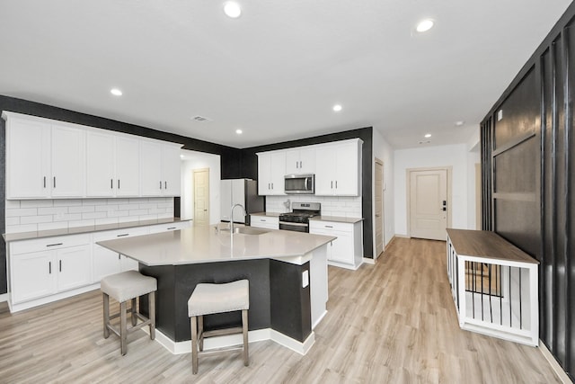 kitchen with light wood-style flooring, white cabinetry, light countertops, appliances with stainless steel finishes, and an island with sink