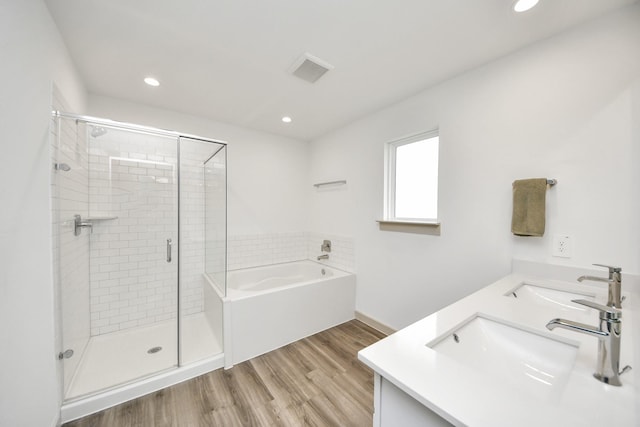 full bath featuring wood finished floors, a sink, visible vents, a bath, and double vanity