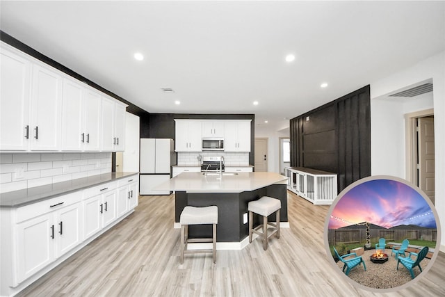 kitchen with stainless steel appliances, a sink, visible vents, white cabinetry, and a center island with sink