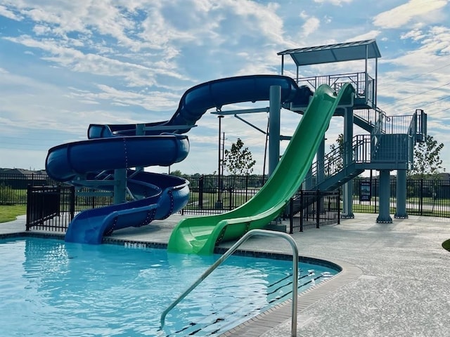 view of swimming pool featuring a water slide, playground community, and fence