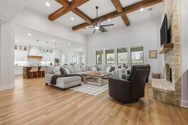 living room with a towering ceiling, a stone fireplace, light wood-style flooring, and beam ceiling