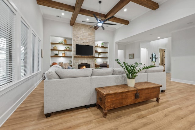 living area with beam ceiling, a stone fireplace, light wood-style flooring, and baseboards