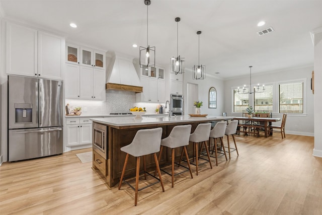 kitchen with stainless steel appliances, visible vents, glass insert cabinets, premium range hood, and a large island with sink