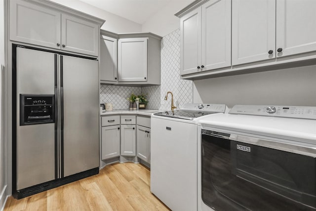 washroom featuring a sink, light wood finished floors, washing machine and clothes dryer, and cabinet space