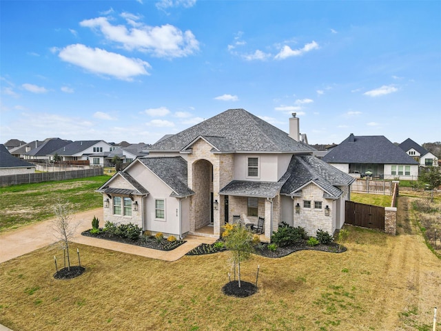 french provincial home with stone siding, a front yard, fence, and a residential view