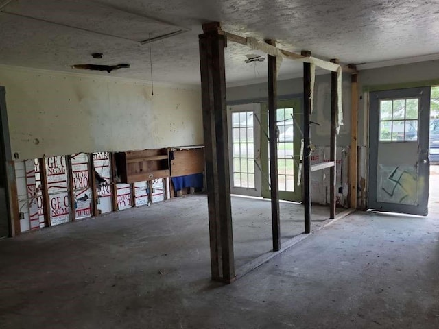 misc room featuring attic access, ornamental molding, a textured ceiling, and unfinished concrete floors