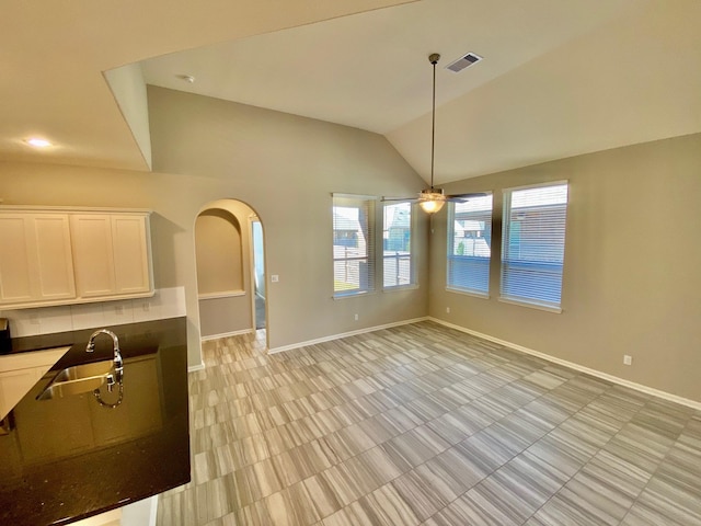 interior space featuring baseboards, arched walkways, visible vents, vaulted ceiling, and a sink