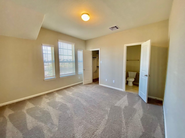 unfurnished bedroom with carpet floors, a walk in closet, visible vents, ensuite bathroom, and baseboards