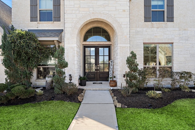 property entrance with stone siding, french doors, brick siding, and a lawn