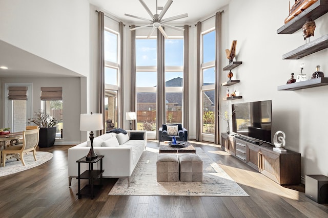 living room featuring a towering ceiling, baseboards, and wood finished floors