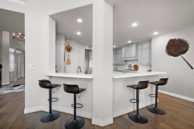 kitchen featuring a breakfast bar area, light countertops, decorative backsplash, a sink, and a peninsula